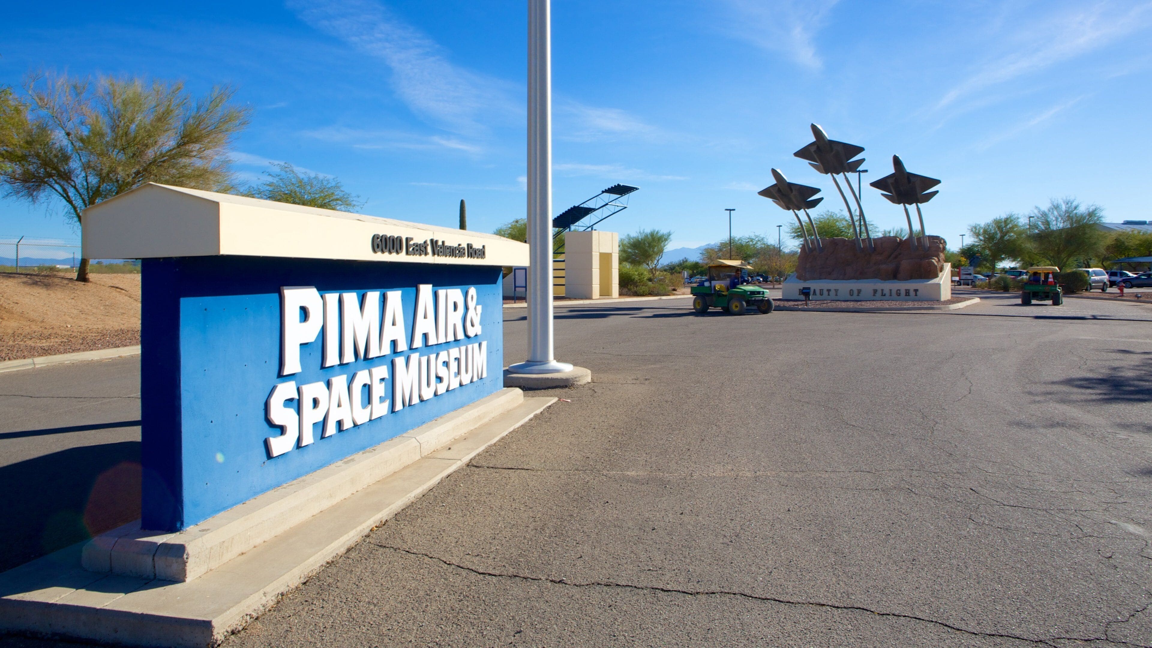 A sign for the Pima Air & Space Museum with a clear sky and a few vehicles in the background.