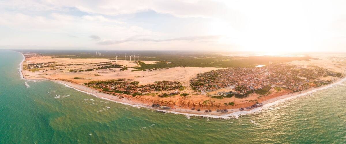 An aerial view of a coastal town with a beach, wind turbines, and a dense residential area.