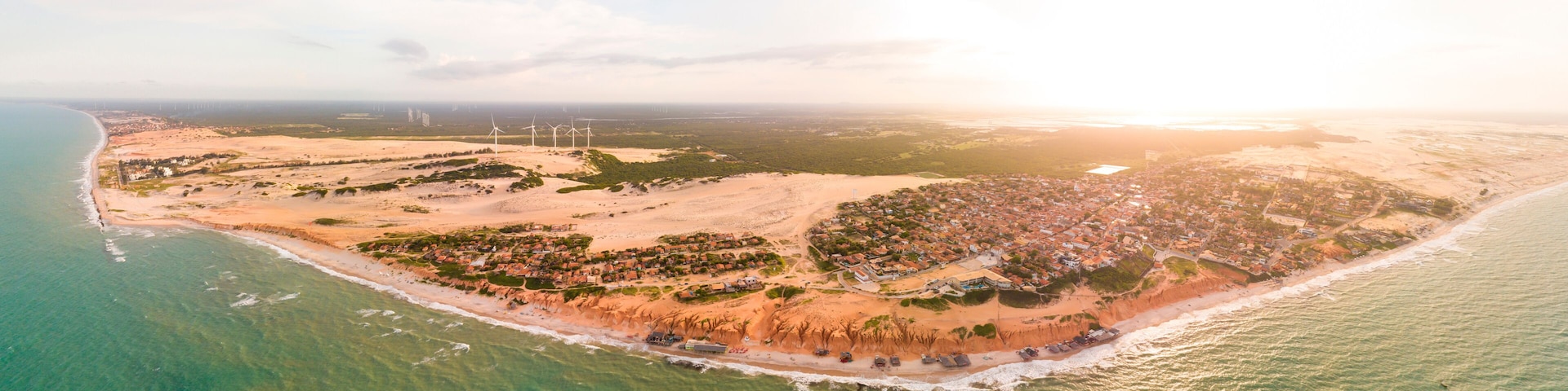 An aerial view of a coastal town with a beach, wind turbines, and a dense residential area.