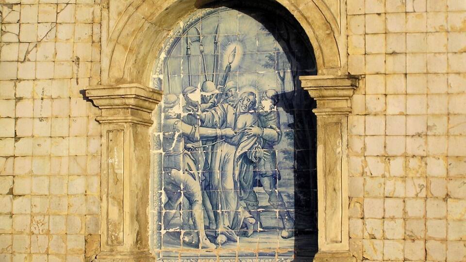 A weathered mural with figures in blue and white tiles, framed by an arched stone structure.