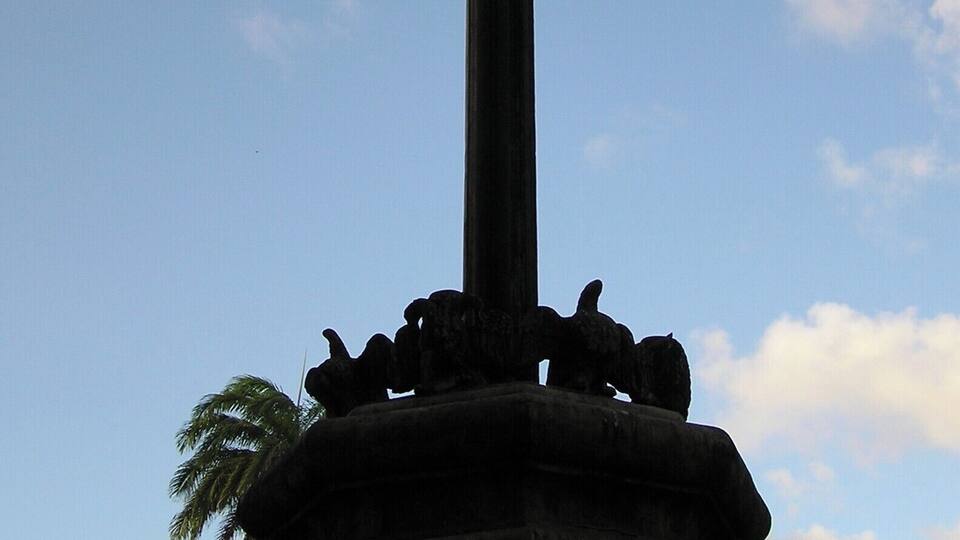 A cross monument with a base sculpture, set against a clear sky.