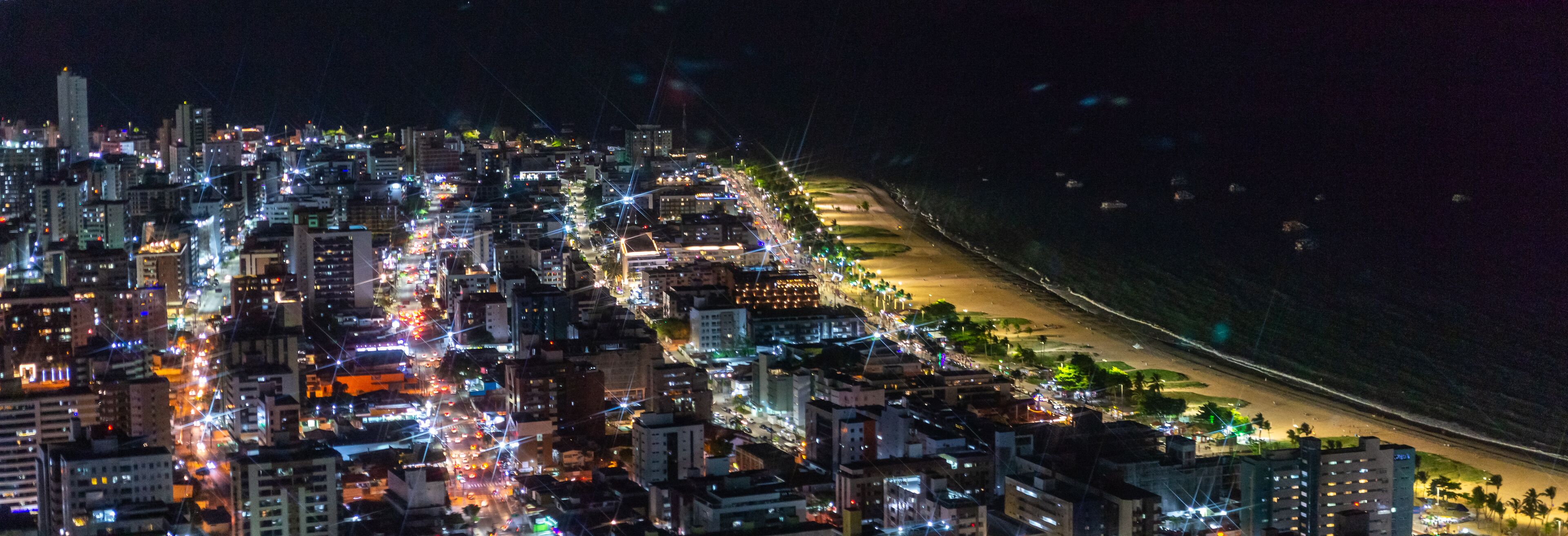 A nighttime cityscape with a densely packed urban area, a beach, and a coastline.