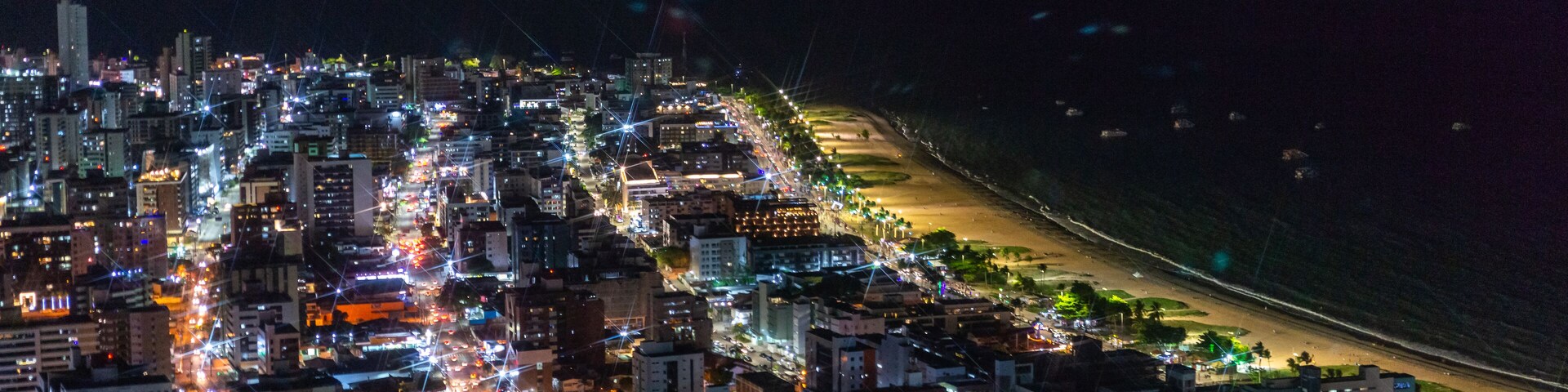 A nighttime cityscape with a densely packed urban area, a beach, and a coastline.