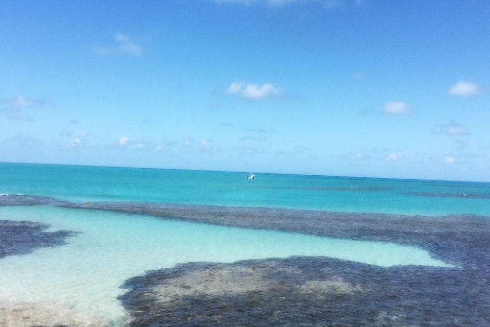 Une plage avec une eau turquoise et limpide, des formations rocheuses et un parasol bleu.