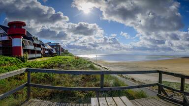 A beach with a wooden boardwalk, a red and white lighthouse, and a telescope.