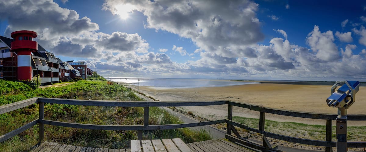 A beach with a wooden boardwalk, a red and white lighthouse, and a telescope.