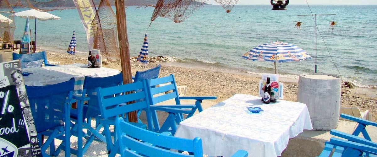 A beachside café with blue chairs and tables, a thatched umbrella, and a netted fishing area.