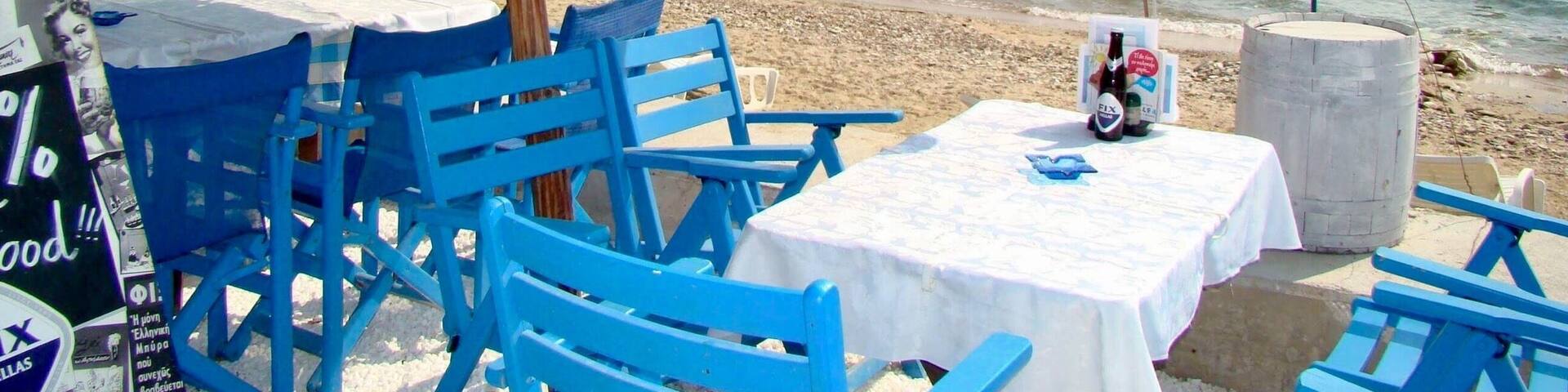 A beachside café with blue chairs and tables, a thatched umbrella, and a netted fishing area.