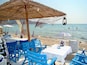 A beachside café with blue chairs and tables, a thatched umbrella, and a netted fishing area.