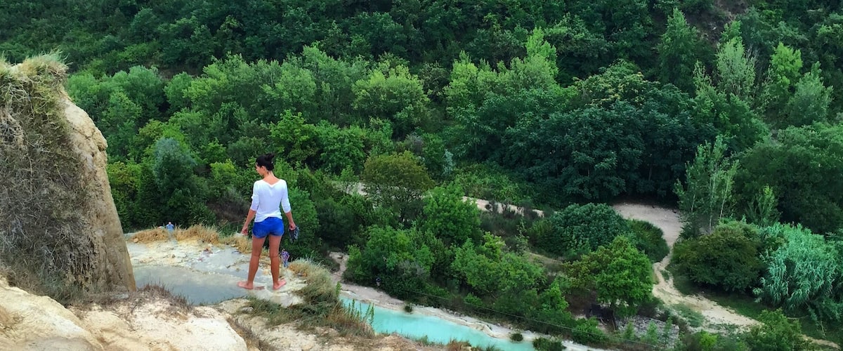 A person standing on a rocky outcrop overlooking a turquoise river and dense forest.