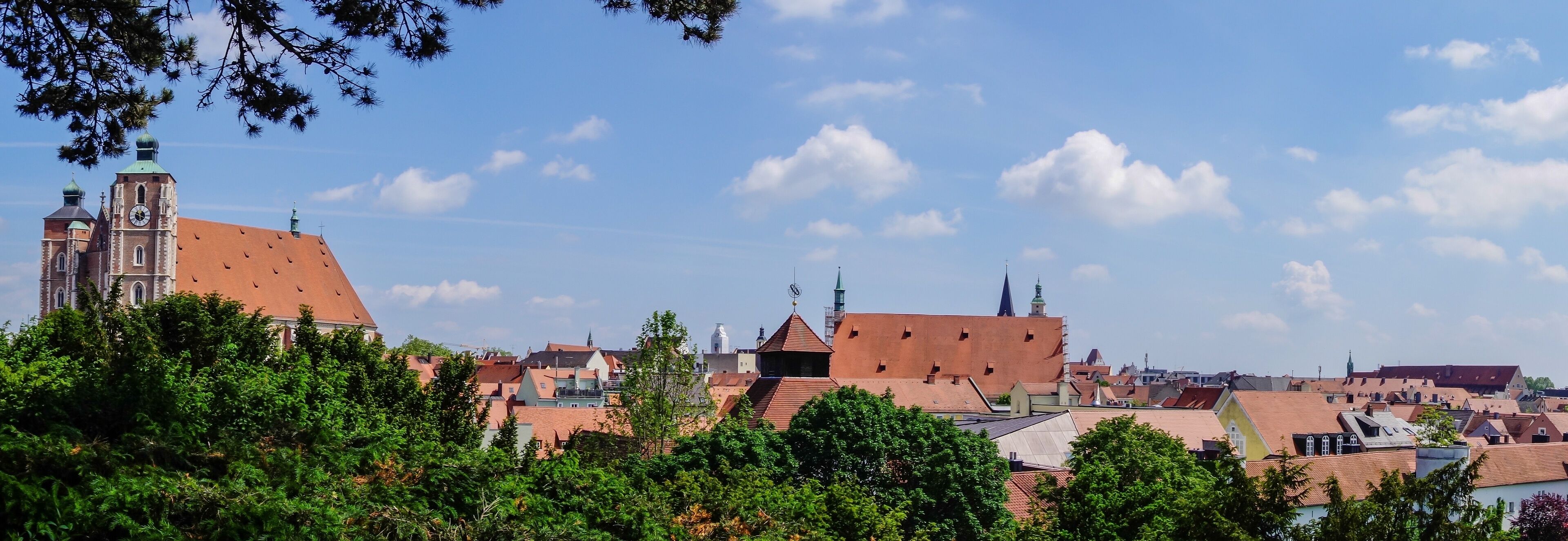 A town with red-roofed buildings, a prominent church with a clock tower, and green trees in the foreground.