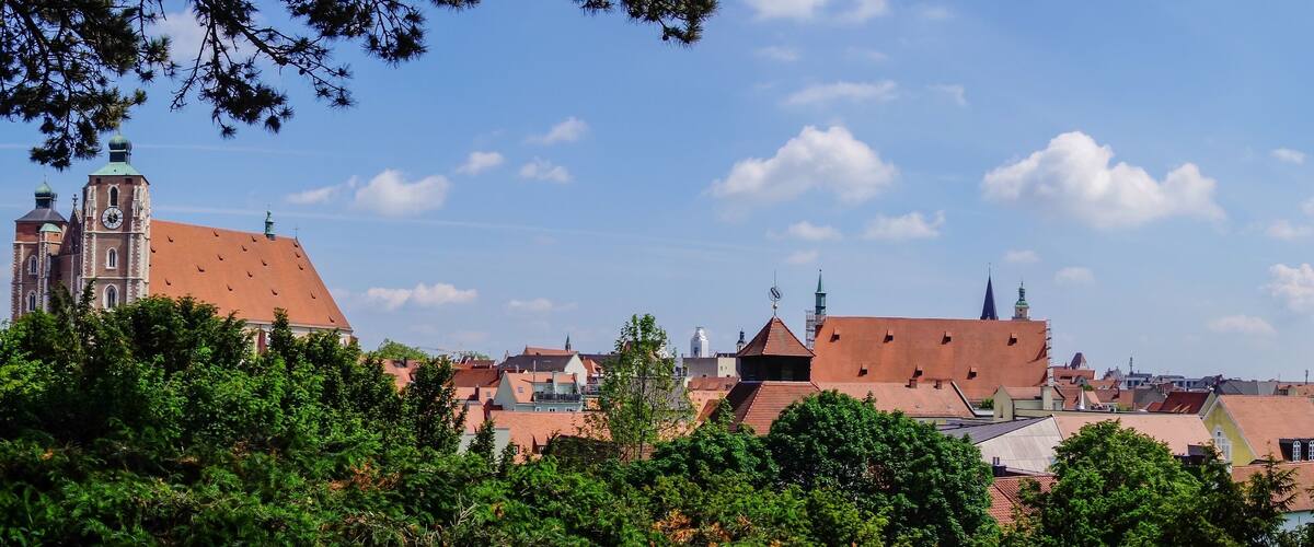 A town with red-roofed buildings, a prominent church with a clock tower, and green trees in the foreground.