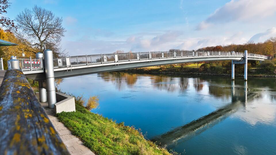 A white bridge over a calm river, surrounded by greenery and autumn trees.