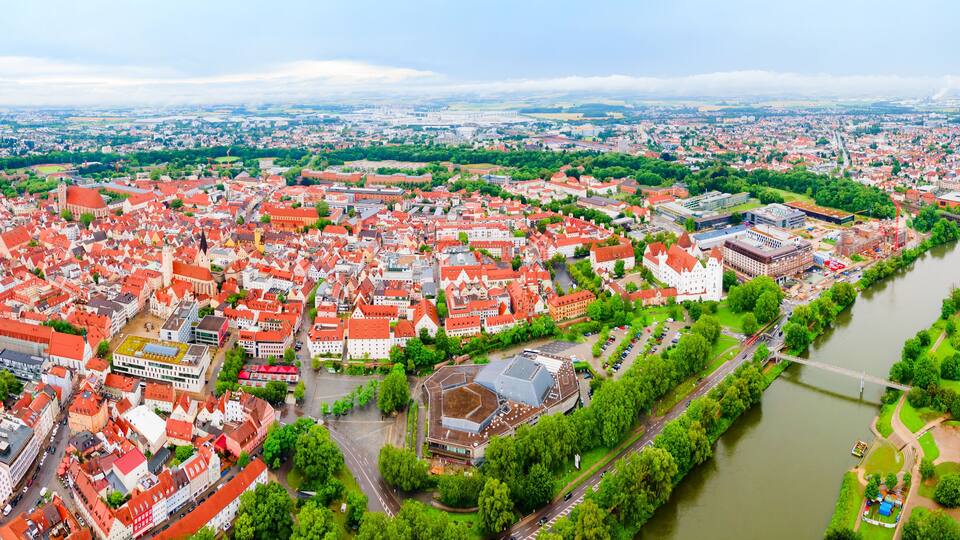 An aerial view of a historic town with red-roofed buildings, a river, and a bridge.