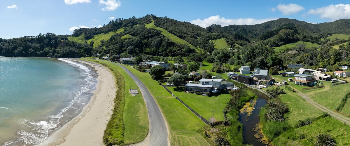 A coastal landscape with a beach, a road, and houses on a hillside.