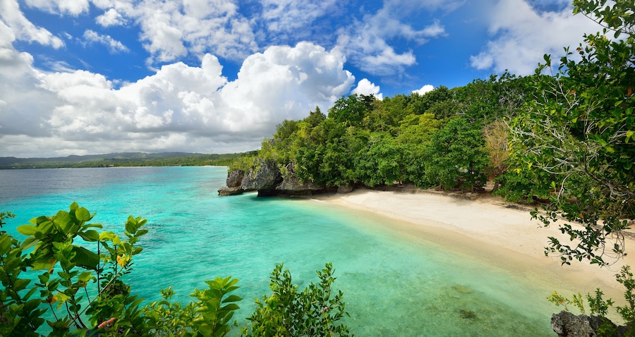 A turquoise beach with clear water, surrounded by lush green vegetation and rocky cliffs.