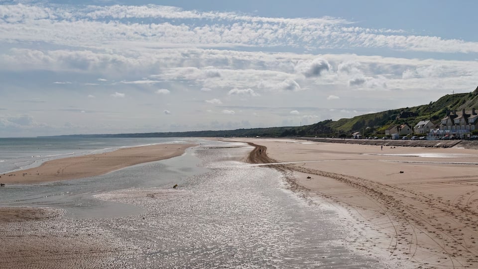 A beach with pebbles and sand, a sandy path, and houses on a hillside.