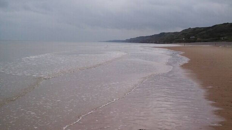 A beach with wet sand and gentle waves under a cloudy sky.