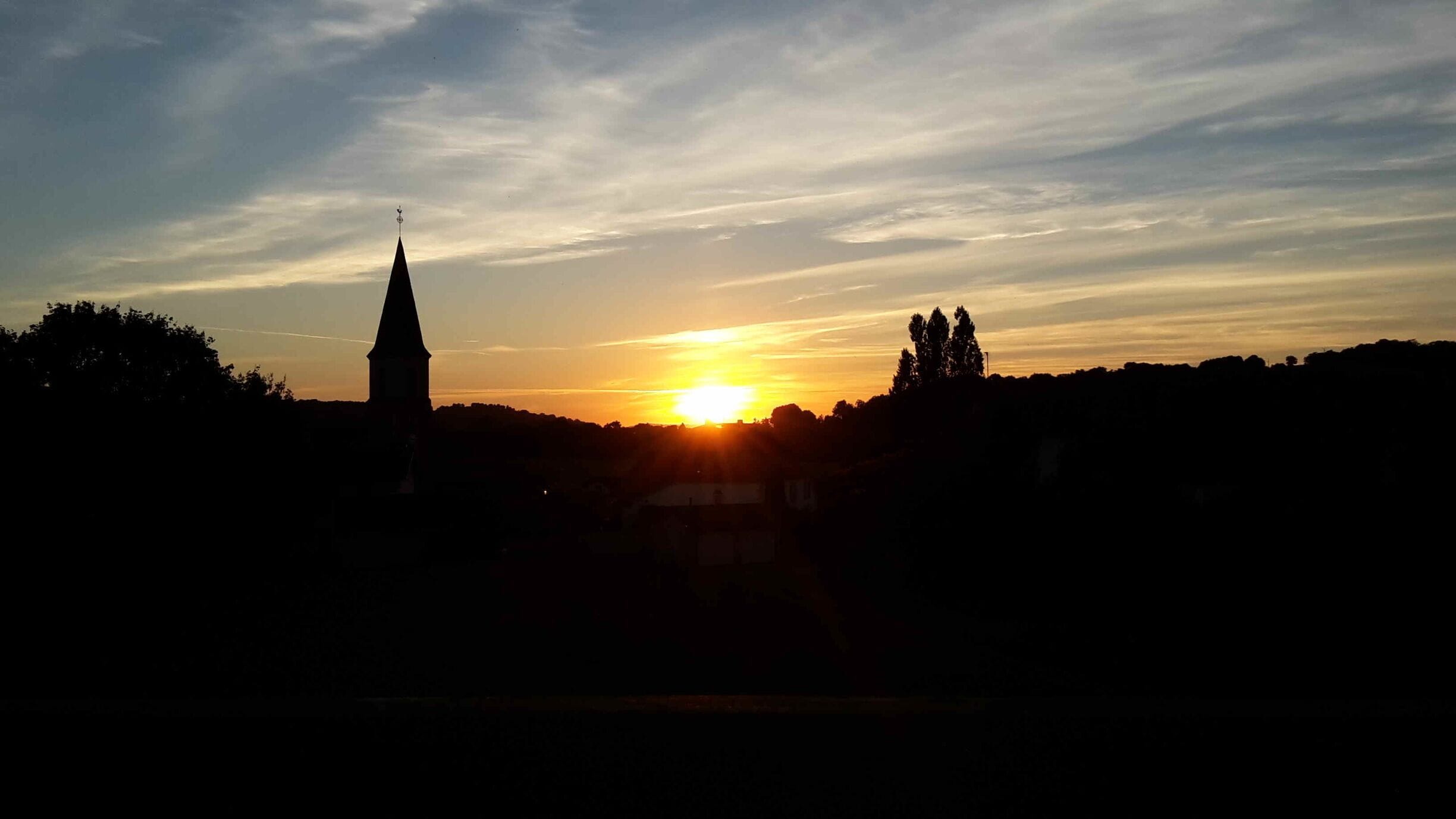 A sunset over a town with a prominent church spire silhouetted against the sky.