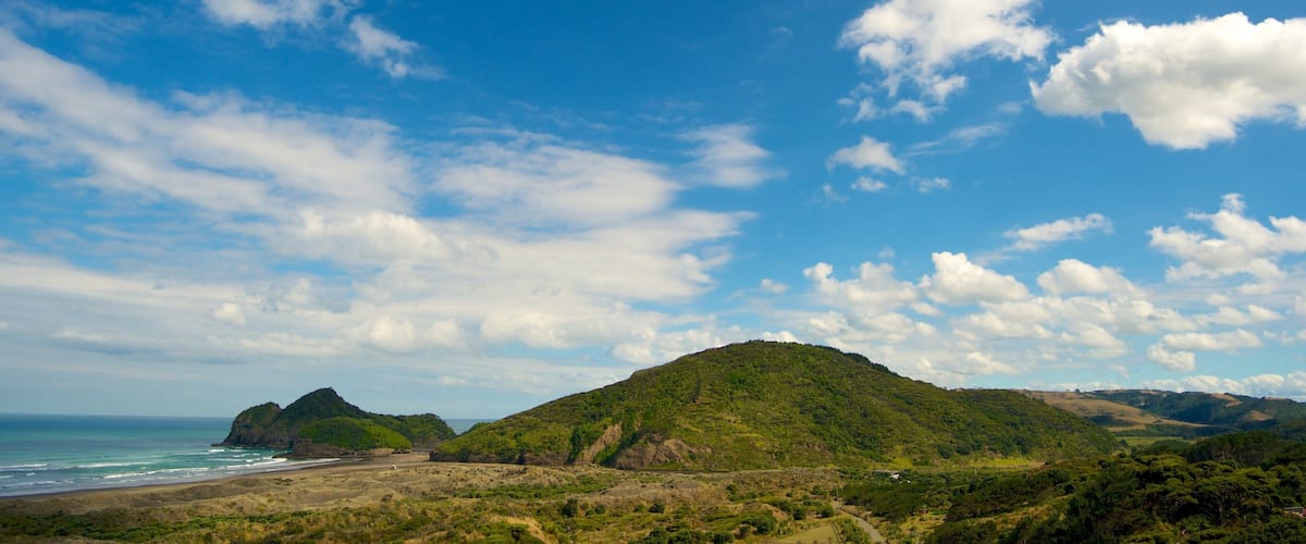 Un paysage côtier avec une plage, une colline et un ciel bleu dégagé parsemé de nuages.