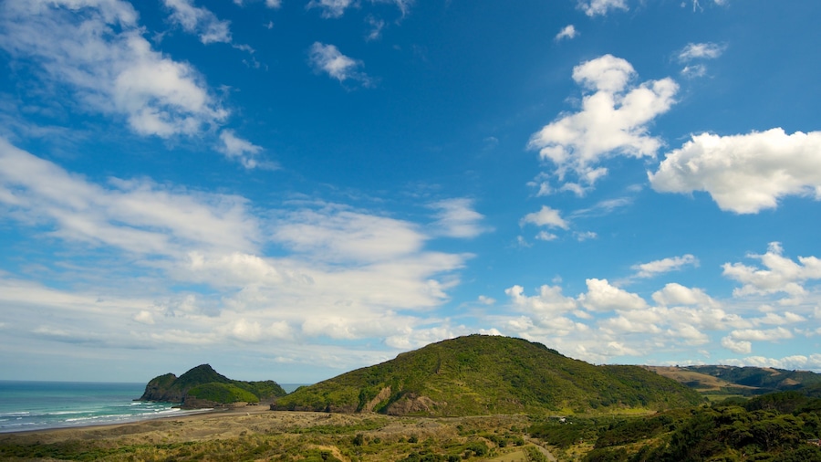 Un paysage côtier avec une plage, une colline et un ciel bleu dégagé parsemé de nuages.