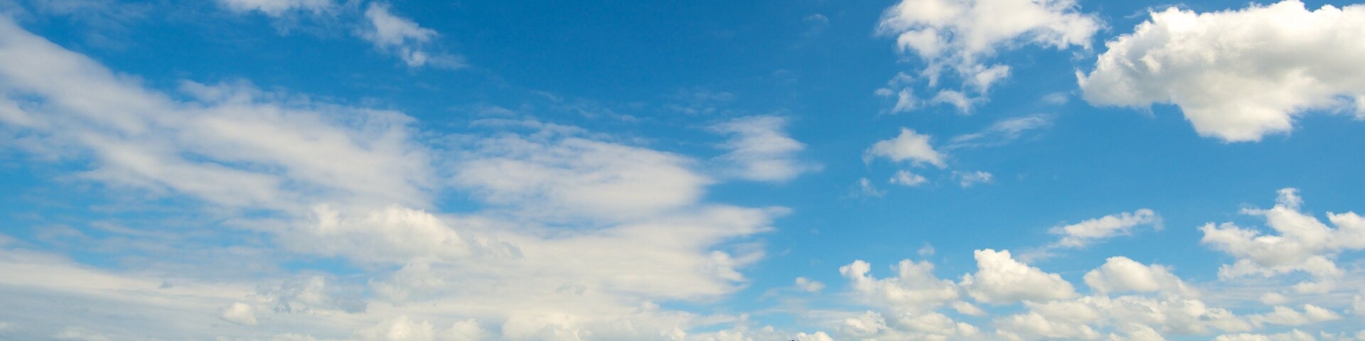 Paisaje costero con playa, colina y cielo azul despejado con nubes.