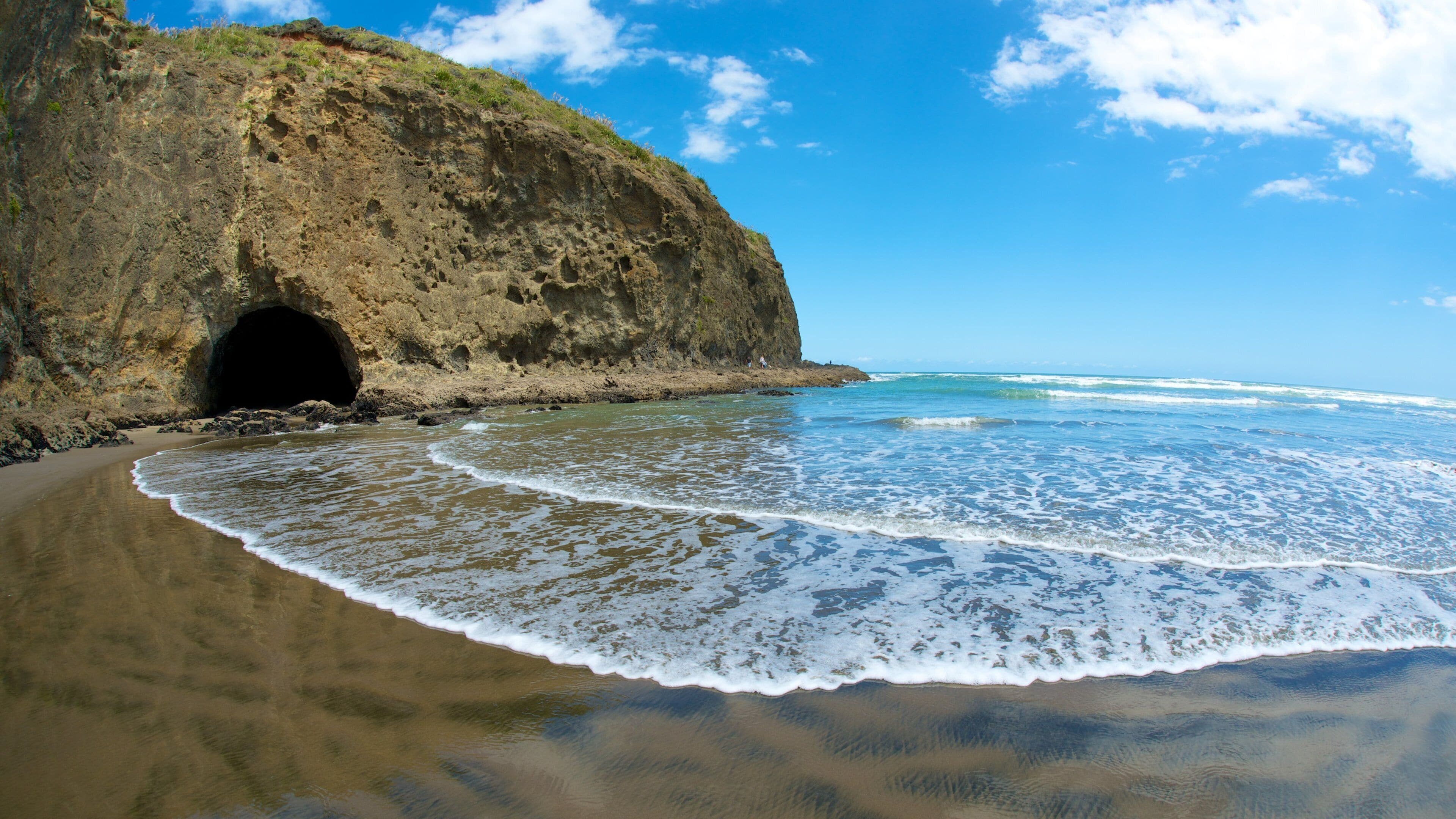 A beach with a rocky cliff and a cave entrance.
