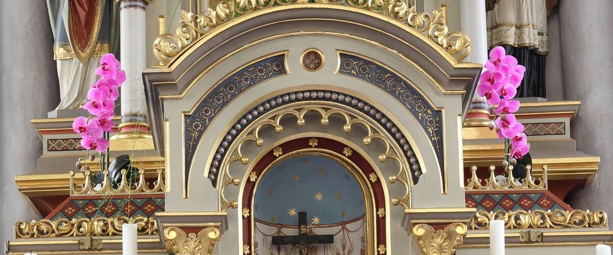 A religious altar with a statue of the Virgin Mary, surrounded by ornate gold decorations and floral patterns.