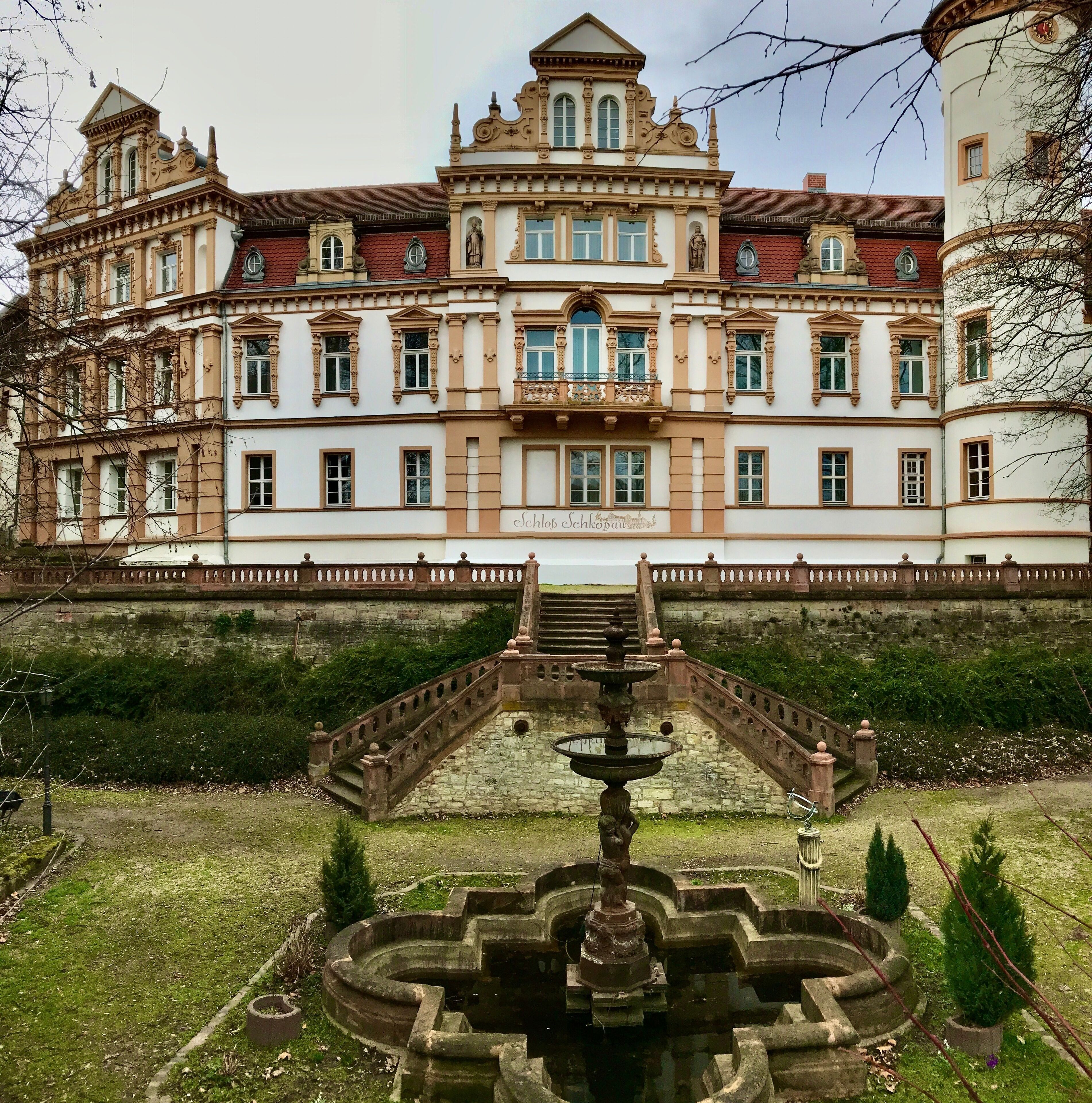 A grand historic building with ornate architecture, a central staircase, and a fountain in the foreground.