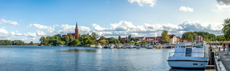 Ein ruhiger Fluss mit anlegenden Booten, eine Kirche mit einem hohen Turm und Wohnhäuser am Ufer.