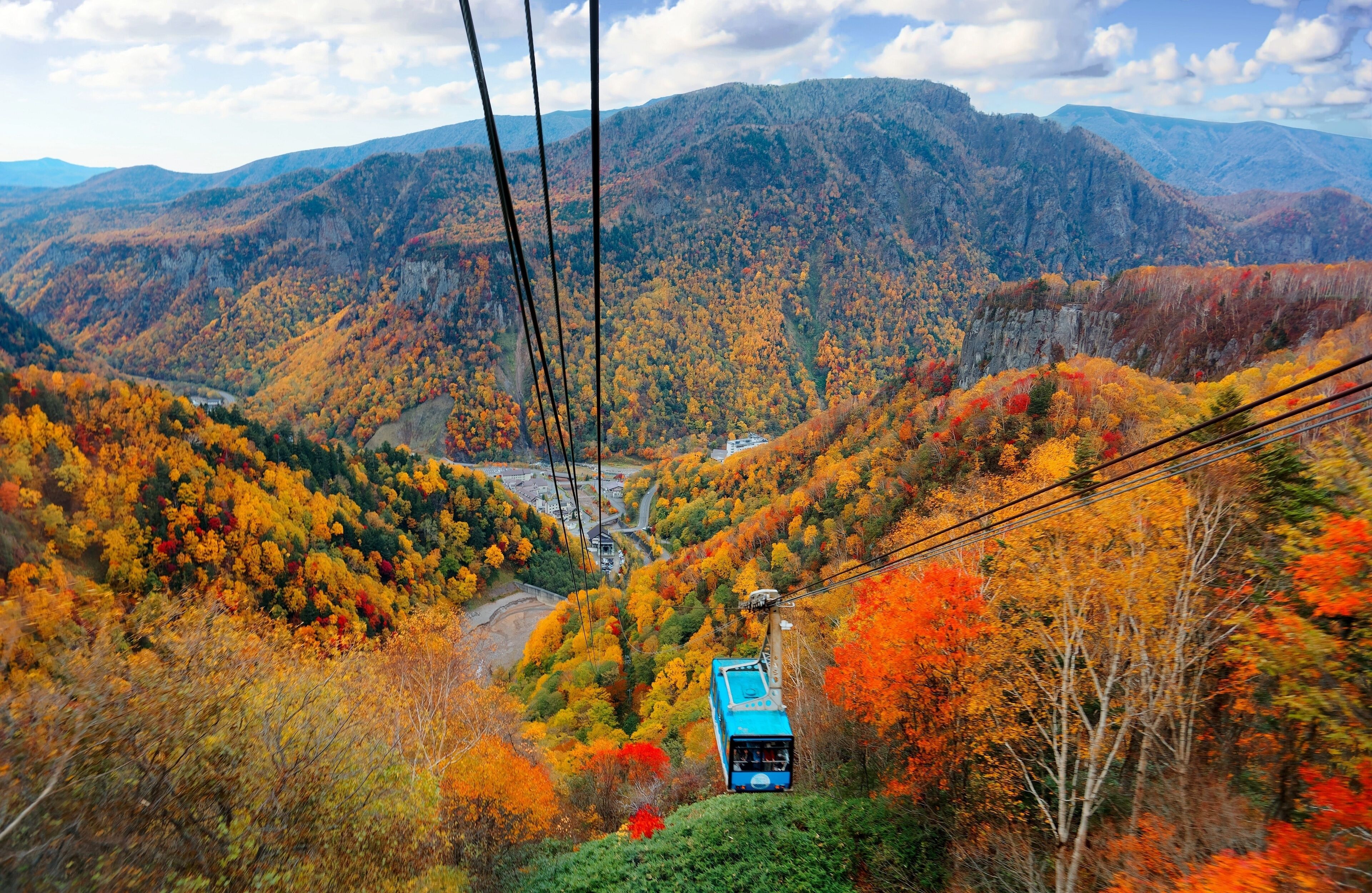 A cable car moving through a mountainous area with autumn foliage.