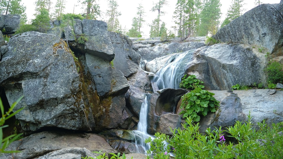 A waterfall cascading over large rocks surrounded by greenery and trees.