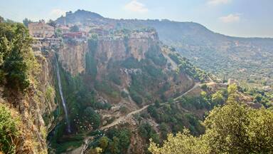Un paysage montagneux avec une cascade, une route sinueuse et des bâtiments adossés à la falaise.