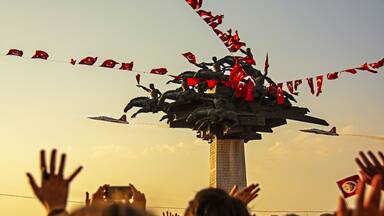 A crowd at a monument with a flag display and a military jet flying overhead.