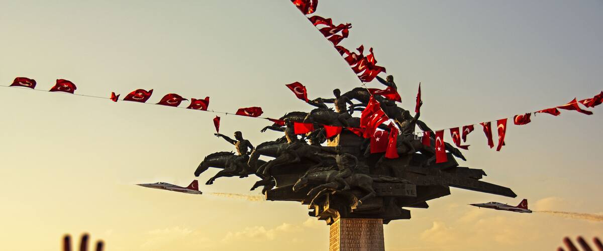 A crowd at a monument with a flag display and a military jet flying overhead.
