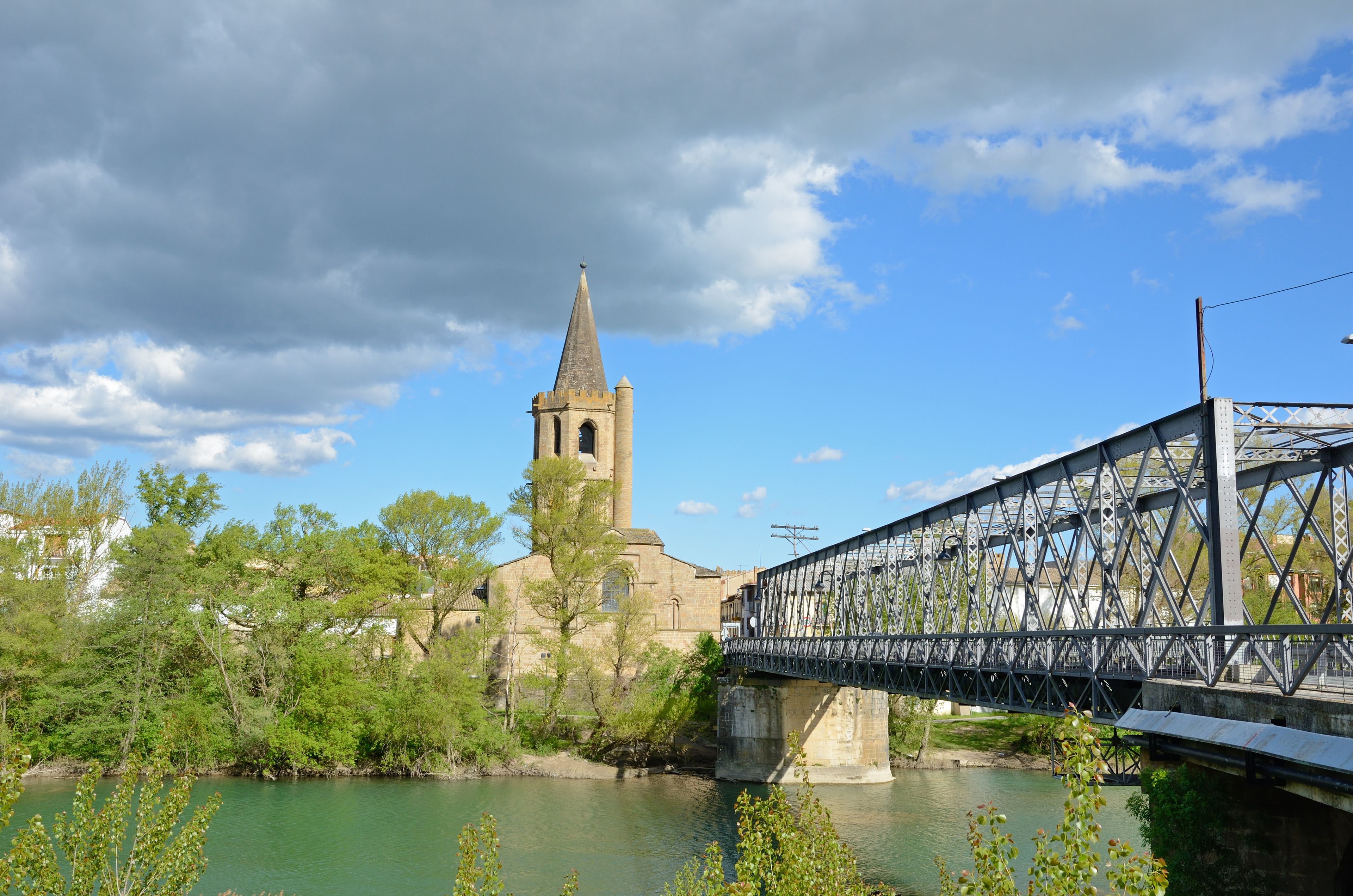 A stone church with a tall tower and a metal bridge over a river.