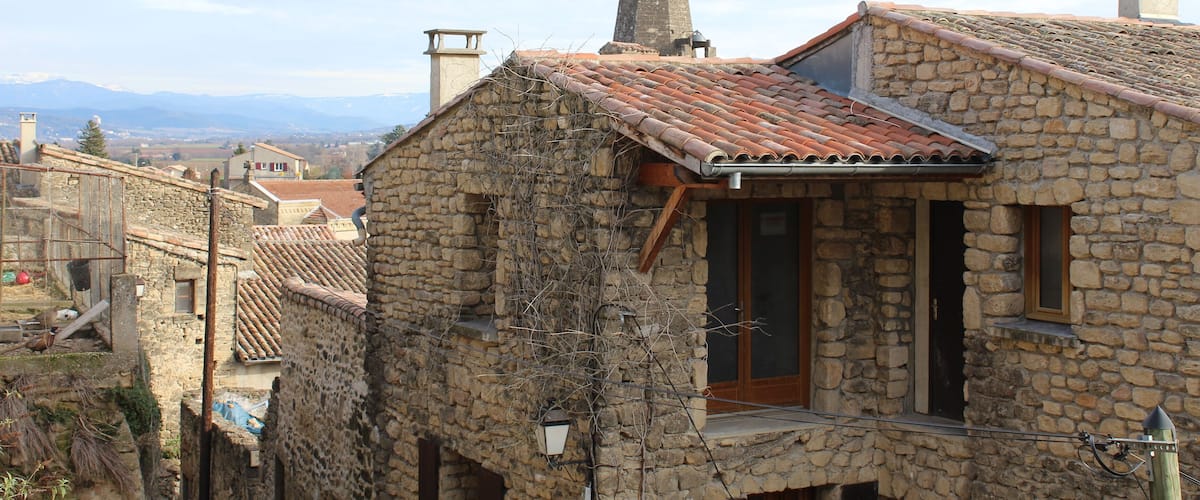 A stone building with a tiled roof and a church steeple in the background.