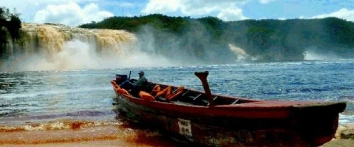 A boat on a sandy shore near a waterfall.