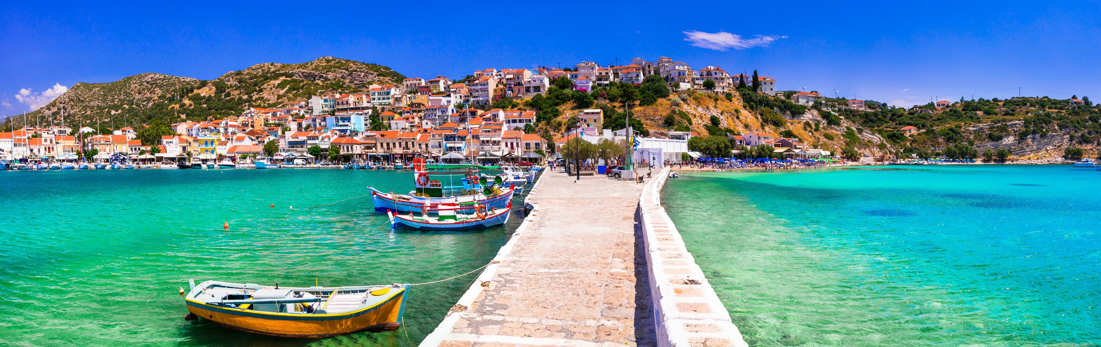 A coastal town with a pier, boats, and a hillside with buildings.