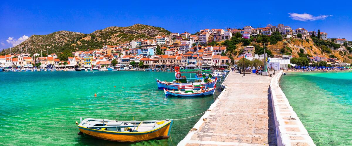 A coastal town with a pier, boats, and a hillside with buildings.