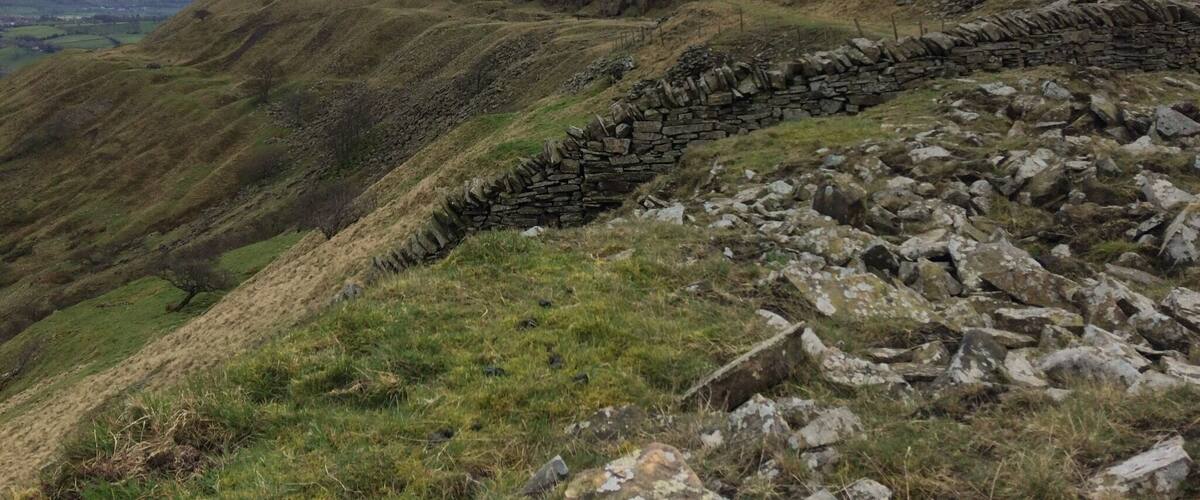 A stone wall on a hillside with a valley in the background.
