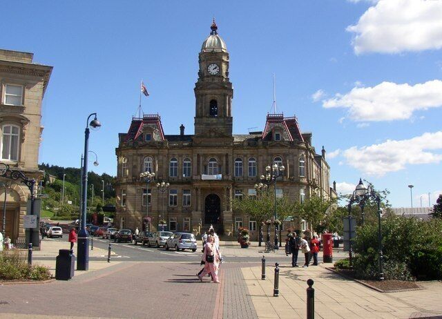 Town Hall, Dewsbury. This Town Hall houses both the council offices and two public halls. It was completed in 1889, and was designed by Holton and Fox, of Dewsbury. Mr Fox also designed Morley Town Hall, and he went on to be mayor of Dewsbury in 1894, just one year after being first elected onto the council. It is not clear on the photo (I should have noticed that the pedestrians were in line with it!) but there is a grand flight of steps up to the main entrance on the first floor. The road on the left side of the building was the main road to Leeds, and the one on the right side to Wakefield, but these have now both been intercepted by the ring road.