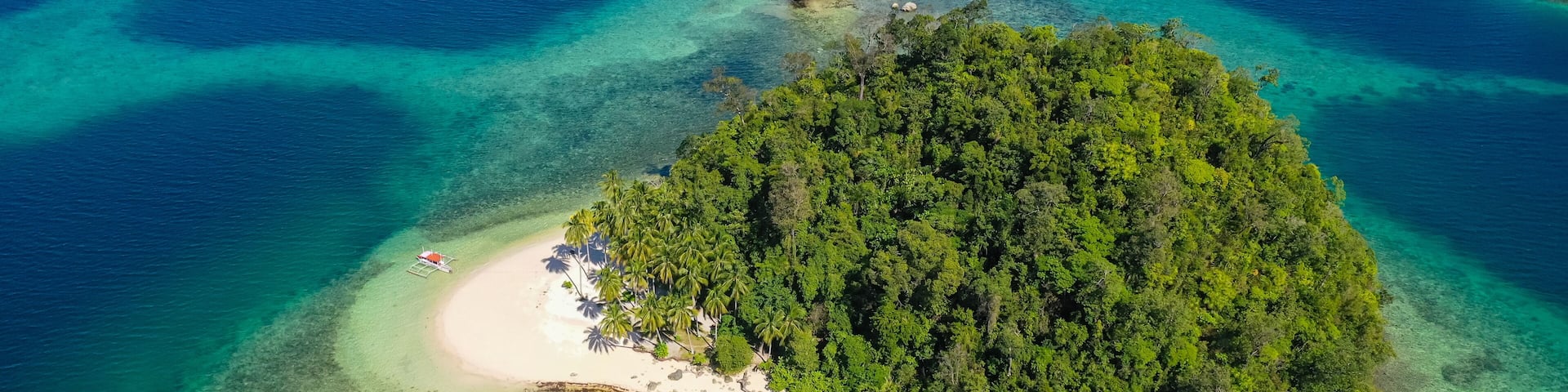 An aerial view of a tropical island with a white sandy beach, dense green forest, and clear turquoise waters.