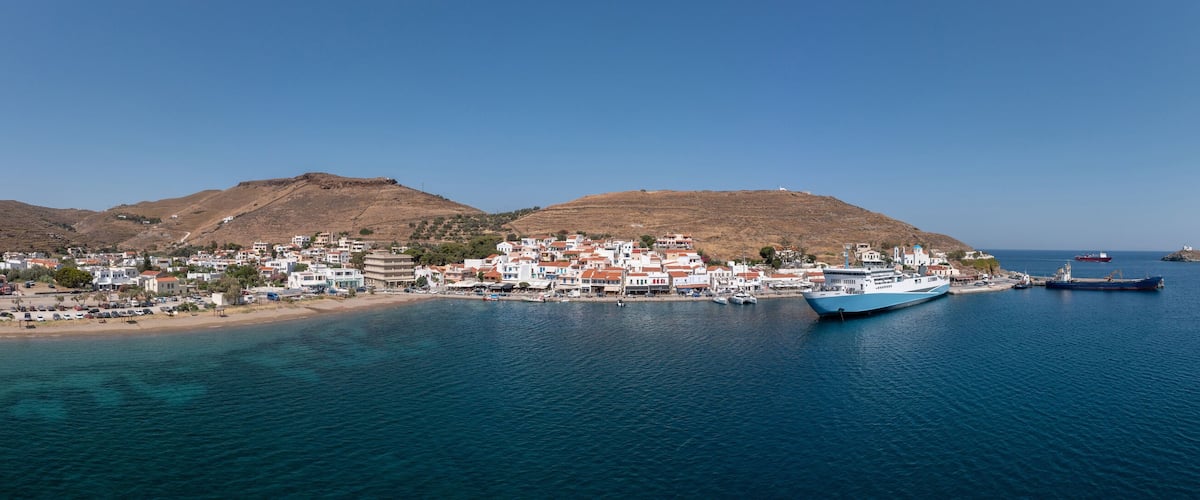 A coastal town with a harbor, boats, and a mountainous backdrop.