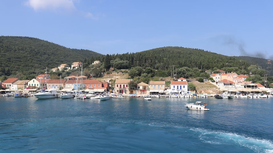 A coastal town with boats docked along the waterfront, surrounded by hills and buildings.