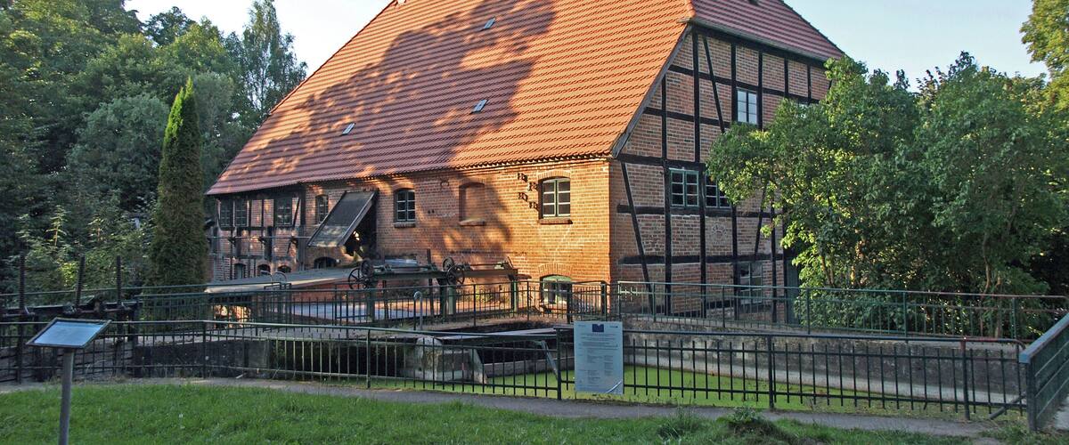 A traditional half-timbered house with a sloped roof, surrounded by a metal fence and greenery.