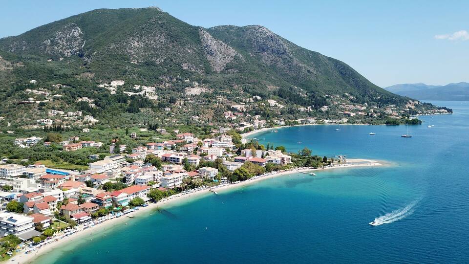 A coastal town with a beach, boats, and mountains in the background.