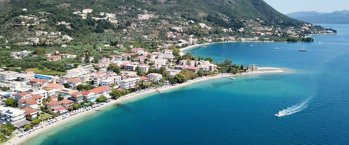 A coastal town with a beach, boats, and mountains in the background.