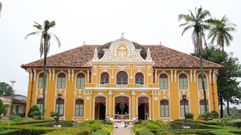 A yellow building with ornate architecture, a statue in front, and palm trees in the background.