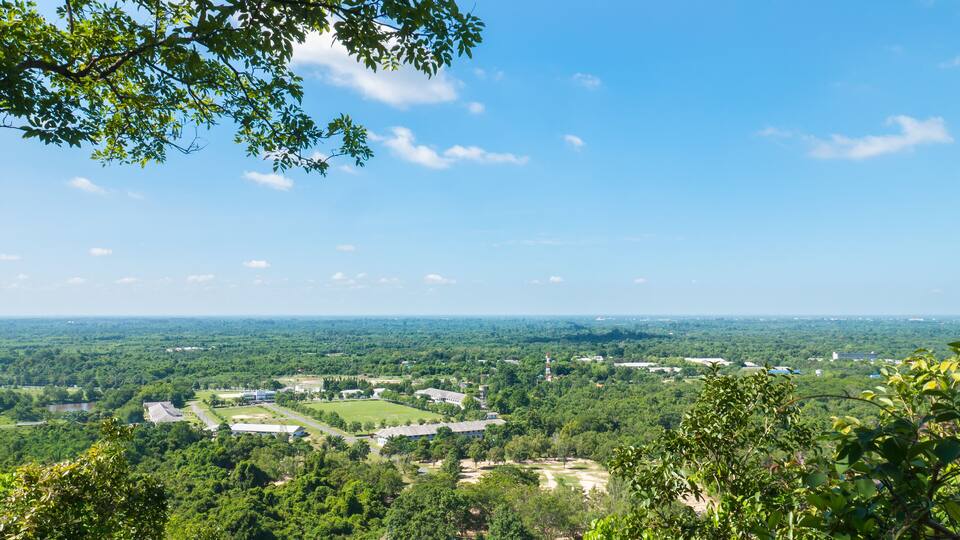 A panoramic view of a lush green landscape with a mix of natural and developed areas, including a large open field and several buildings.
